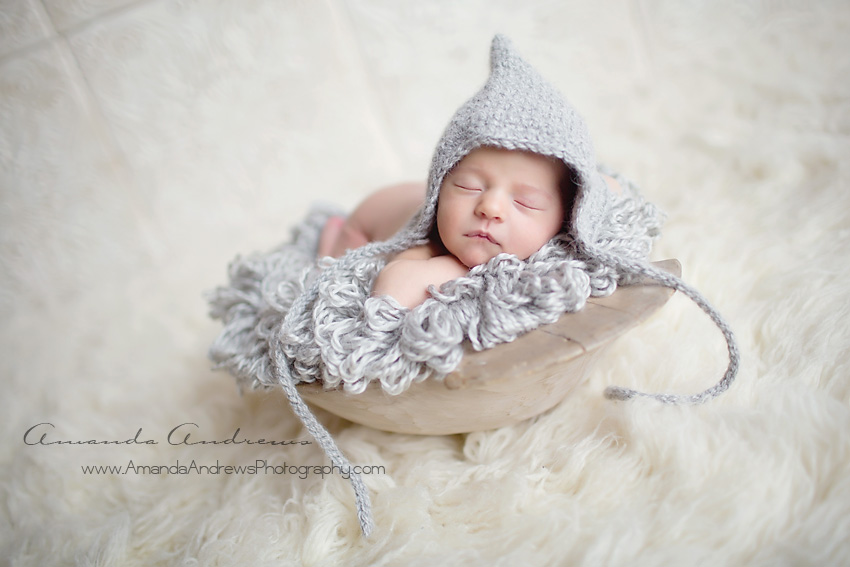 newborn sleeping in wooden bowl with gray hat